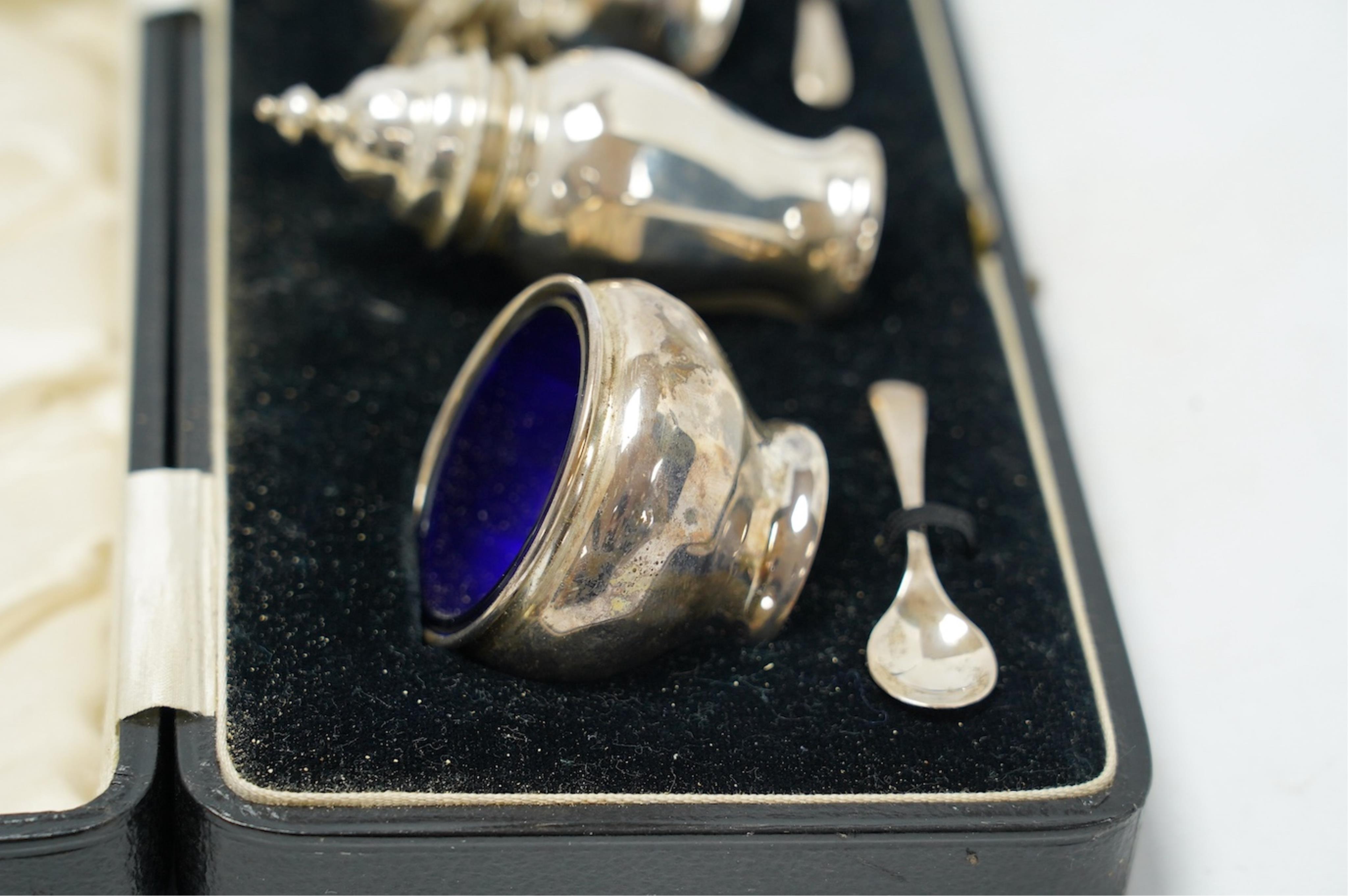 A cased George V silver three piece condiment set, Z. Barraclough & Sons, Chester, 1931, with two associated silver spoons. Condition - fair